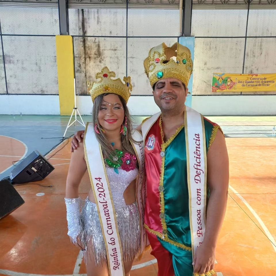 Fotografia da rainha e do rei do Carnaval do Recife, na categoria pessoa com deficiência. Ambos fantasiados na quadra onde ocorreu a eleição.