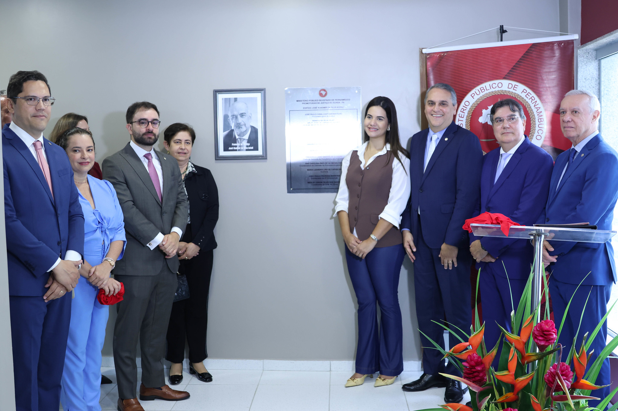 Fotografia de participantes do evento diante da placa que dá nome ao edifício
