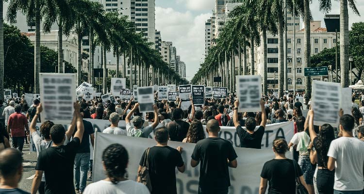 Fotografia de pessoas caminhando em rua em passeata segurando cartazes 