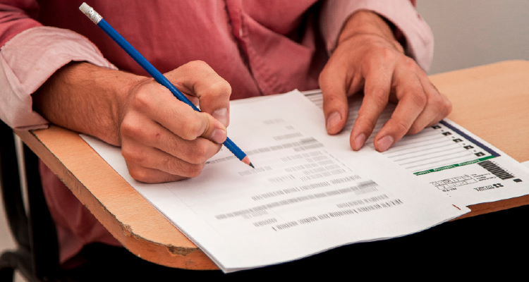 Fotografia de pessoa sentada em banco escolar fazendo prova