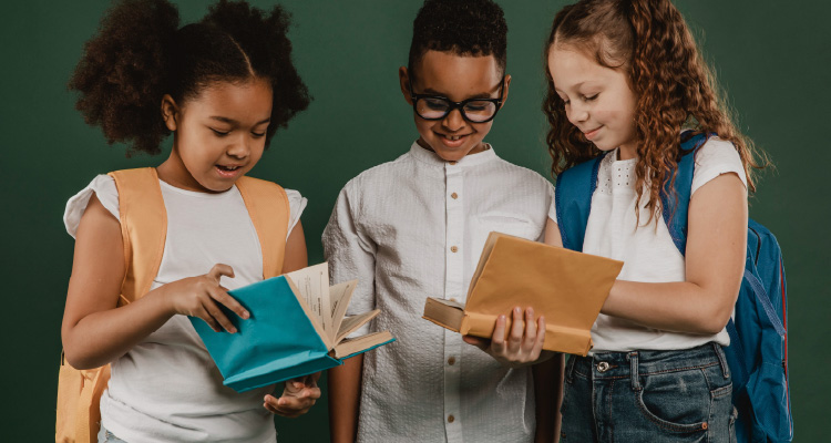 Imagem de três crianças olhando e compartilhando cadernos e sorrindo 