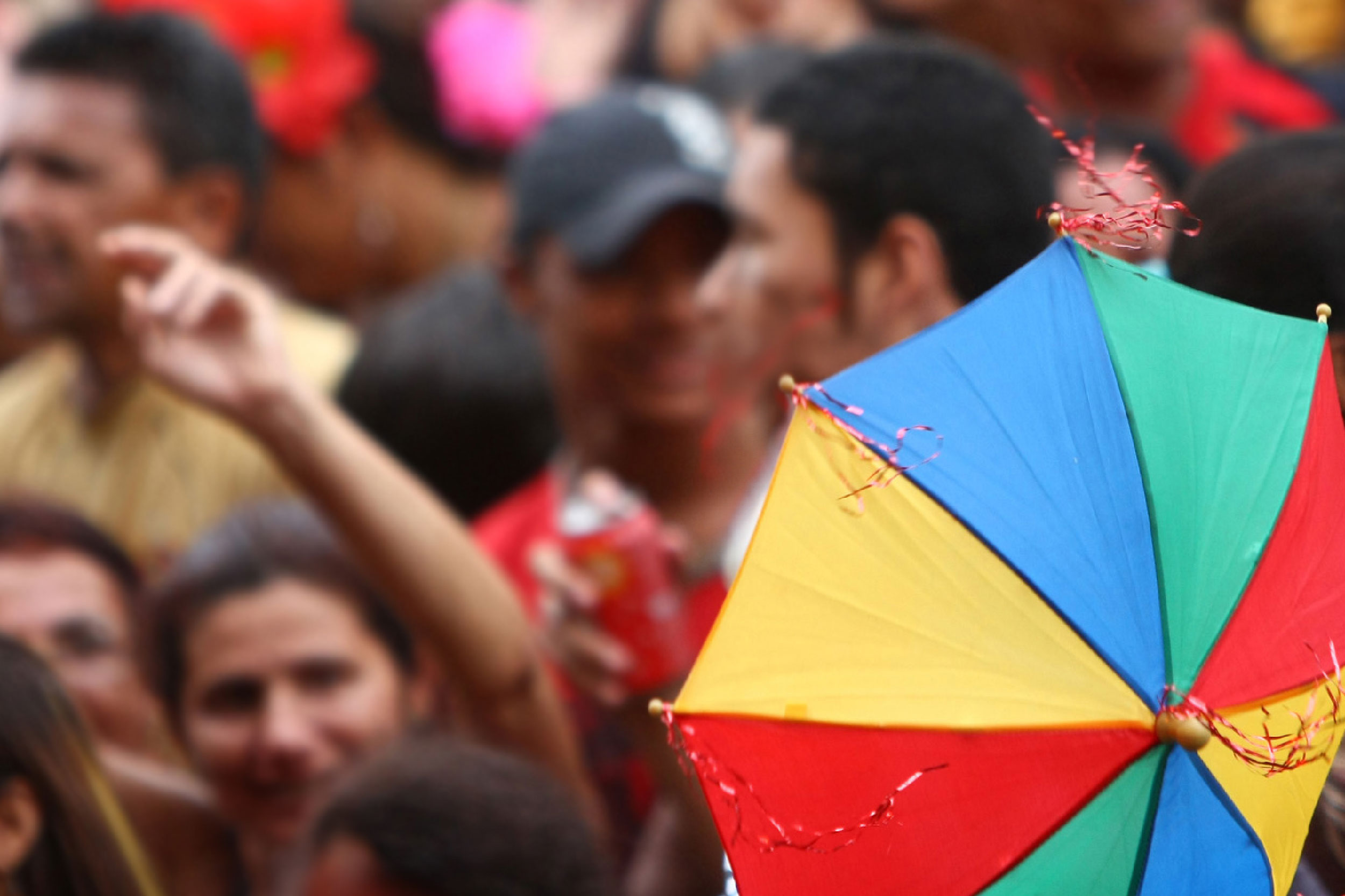 Fotografia de multidão dançando carnaval com destaque para uma sombrinha de frevo em primeiro plano