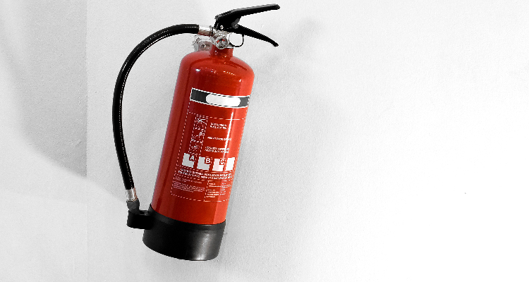 Foto de um extintor de incêndio vermelho em uma parede branca.