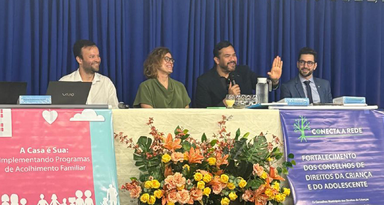 Fotografia de participantes do evento sentados na mesa principal