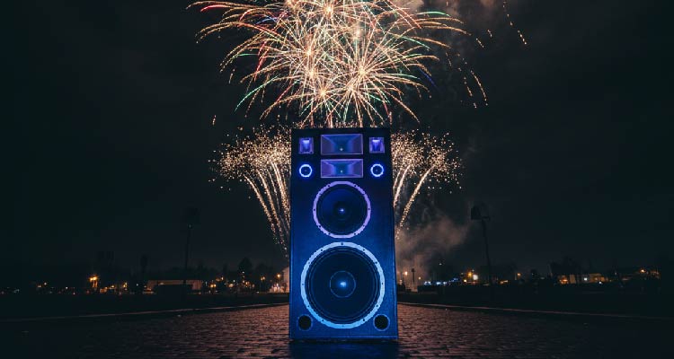 Imagem de caixa de som com fogos de artifício estourando ao longe