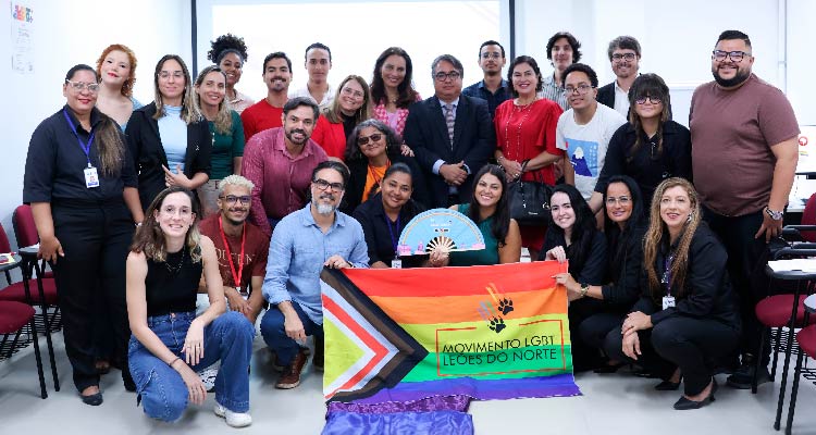 Fotografia de pessoas reunidas posando pra foto com bandeira do movimento LGBTQIAPN+