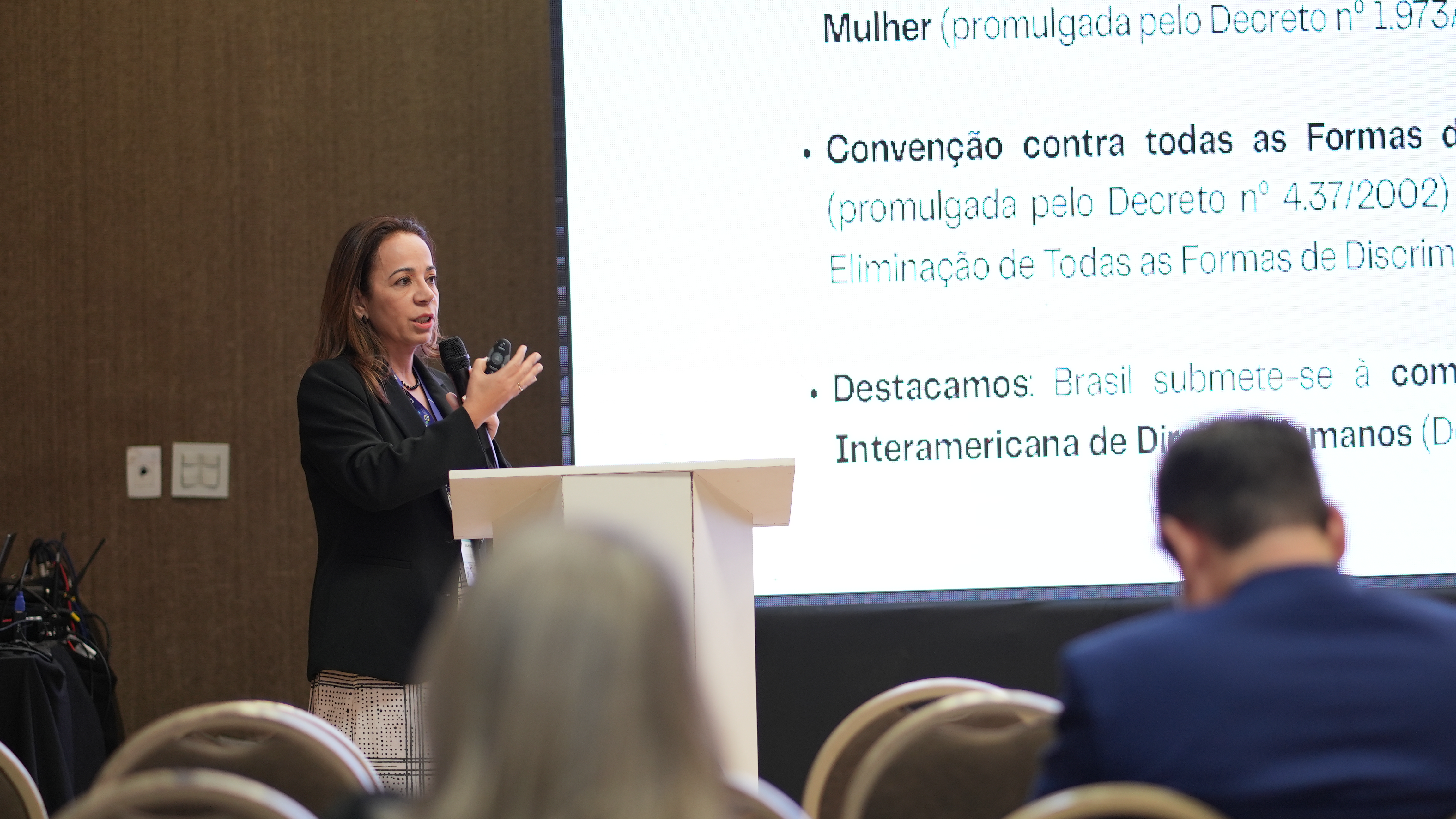 Foto mostra mulher falando em púlpito em direção a plateia.