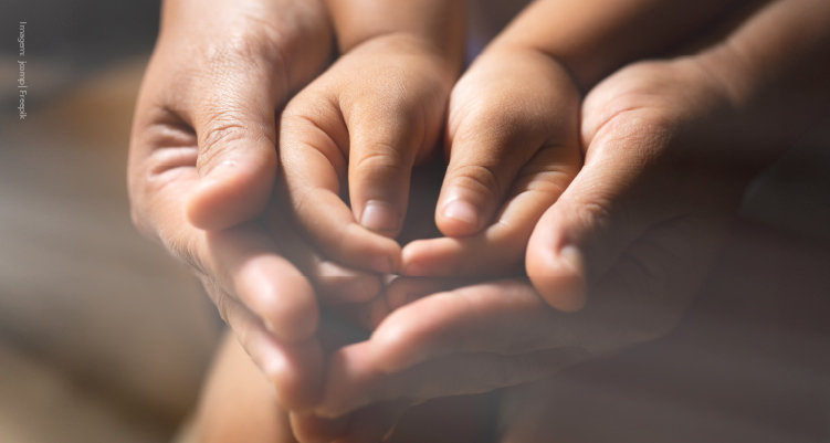 Foto de mãos infantis sendo seguradas por mãos adultas