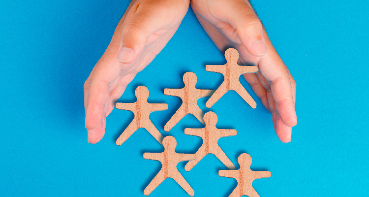 Imagem parcial de mãos sobre fundo azul envolvendo bonecos de madeira em formato de pessoas