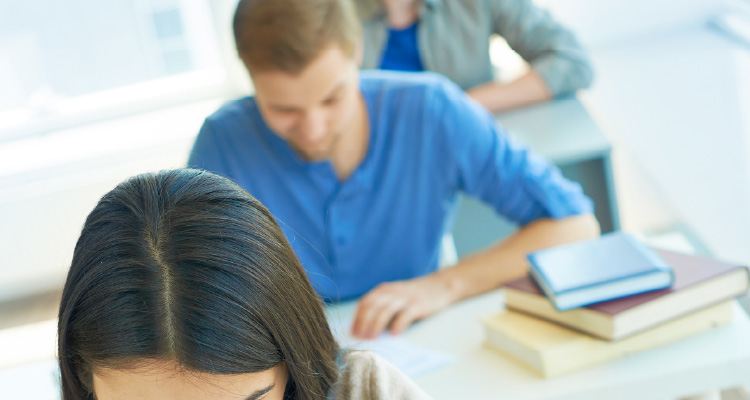 Imagem de pessoas em bancas escolares fazendo prova