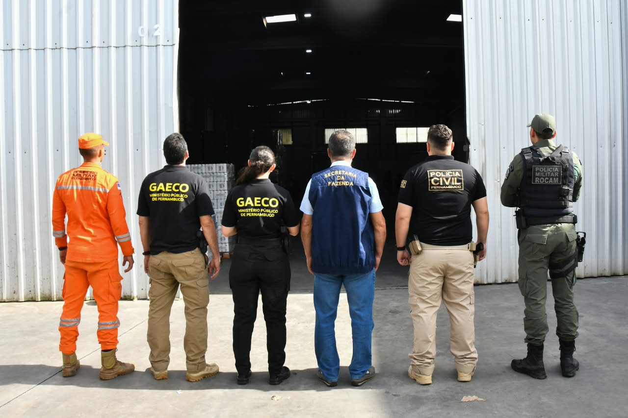 Foto mostra integrantes do Corpo de Bombeiros, Gaeco, Sefaz, Polícia Civil e Polícia Militar em frente à porta do galpão de um dos alvos
