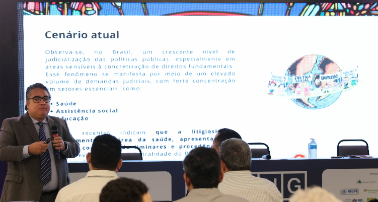 Imagem do PJ Fabiano Pessoa falando ao público diante de projeção de slides