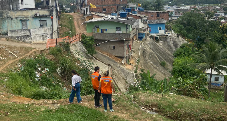 Fotografia de fiscais vistoriando área com casas à beira de uma barreira