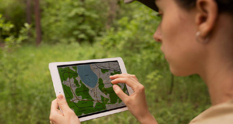 Em um ambiente de vegetação, mulher segura um tablet com as duas mãos e olha fixamente para a tela.