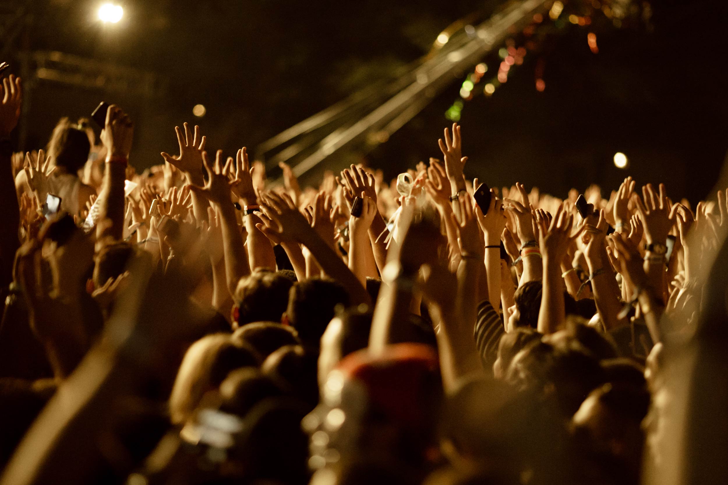 Plateia em show noturno, multidão virada para o palco com os braços levantados.