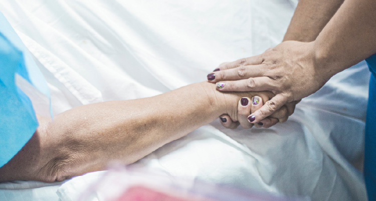 Imagem de mãos segurando outras sobre cama hospitalar