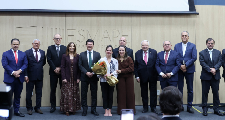 Mulheres e homens de pé reunidos sobre um painel de madeira ao fundo com a inscrição Esmape