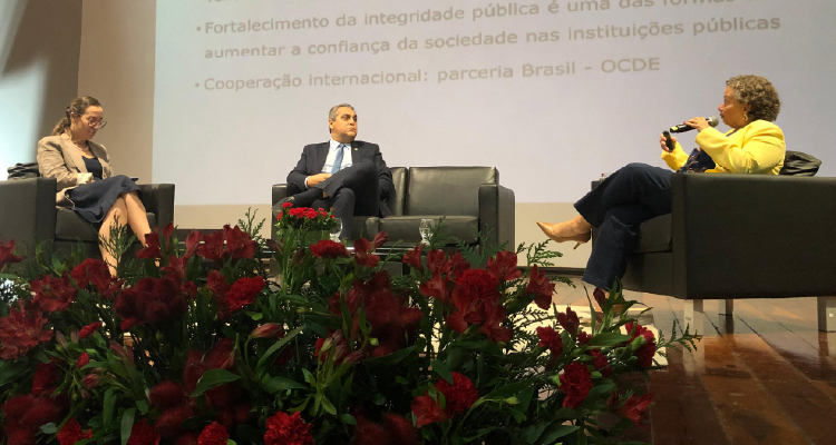 Fotografia de participantes sentados em sala de estar montada no palco