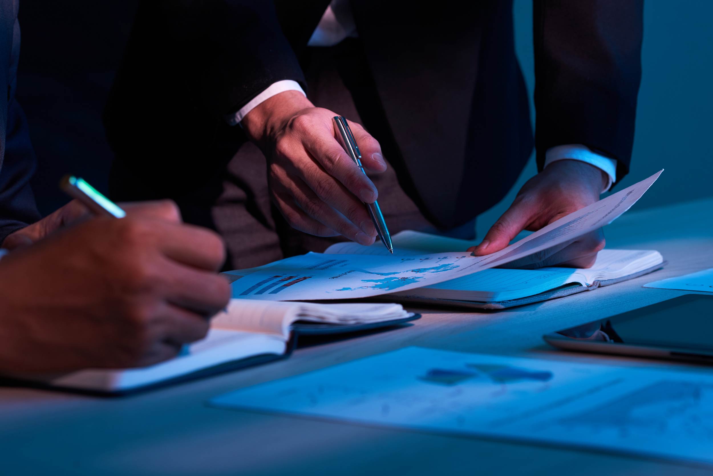 Imagem parcial de mãos assinando documentos sobre uma mesa
