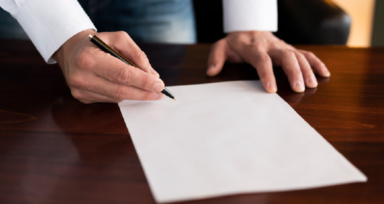Imagem de pessoa assinando papel sobre uma mesa