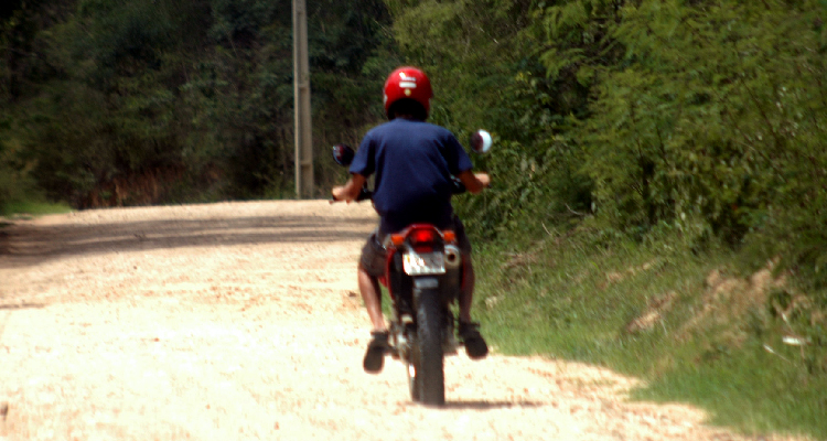 Fotografia de rapaz guiando uma moto em estrada de barro