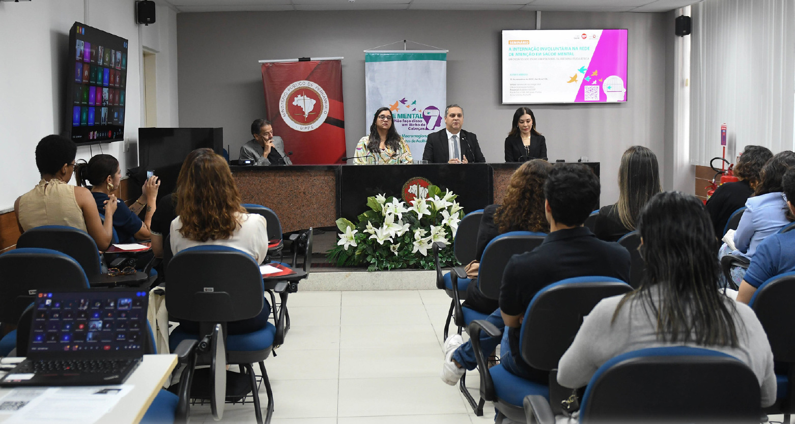 Fotografia do local do evento com plateia diante da mesa principal