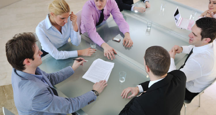 Imagem de pessoas sentadas em volta de uma mesa analisando documentos