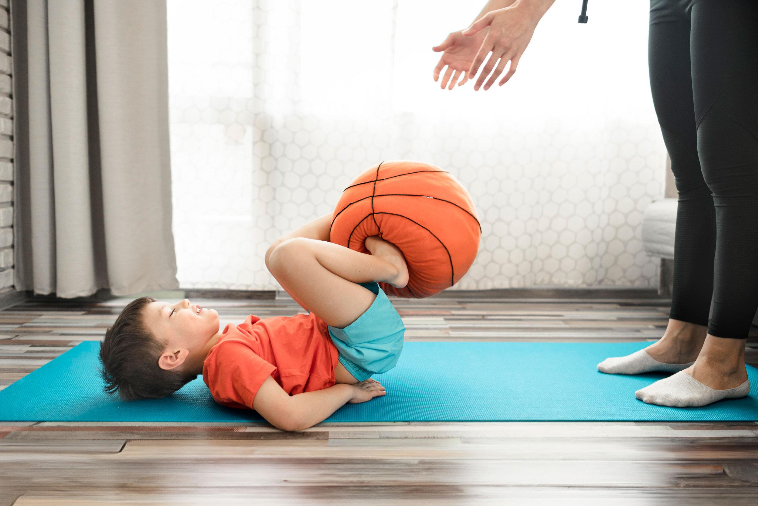 Foto de criança deitada no chão com bola nos pés passando a mãos adultas