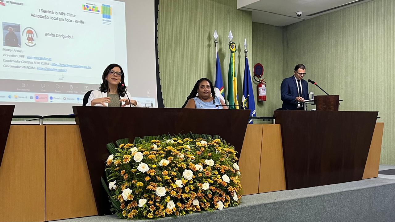 Fotografia de PJ Belize Câmara em primeiro plano na mesa de discussões